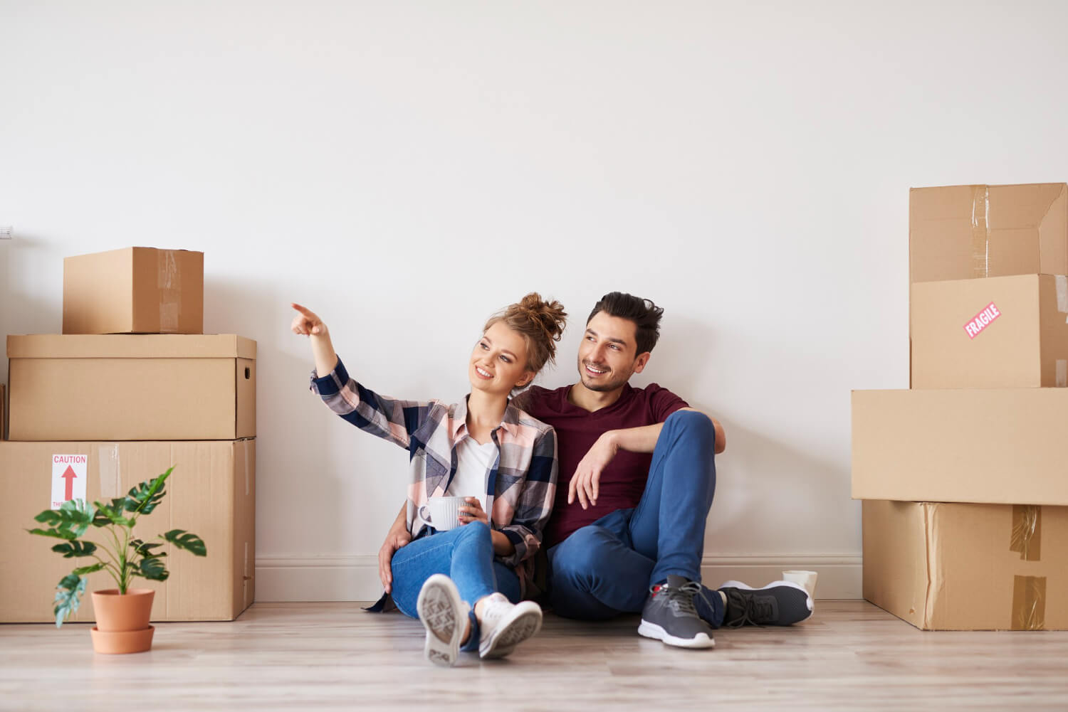 happy couple sitting in the floor of their new home looking out of the window with moving boxes beside them